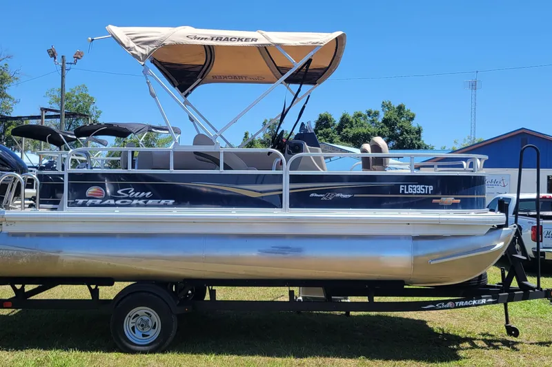 The Image of 2023 Sun Tracker Bass Buggy 18 DLX pontoon boat on trailer, with canopy, parked outdoors. - 1