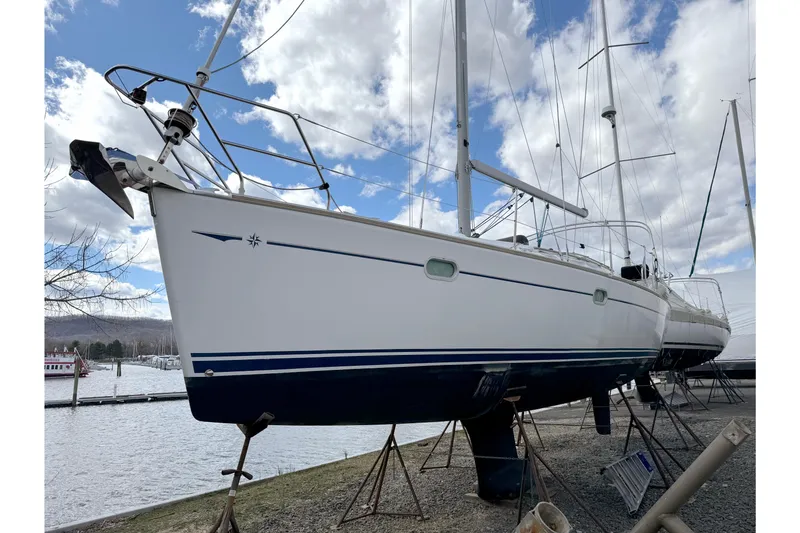 Slide: The Image of 2003 Jeanneau Sun Odyssey 35 sailboat on stands by the water, under a cloudy sky. - 1