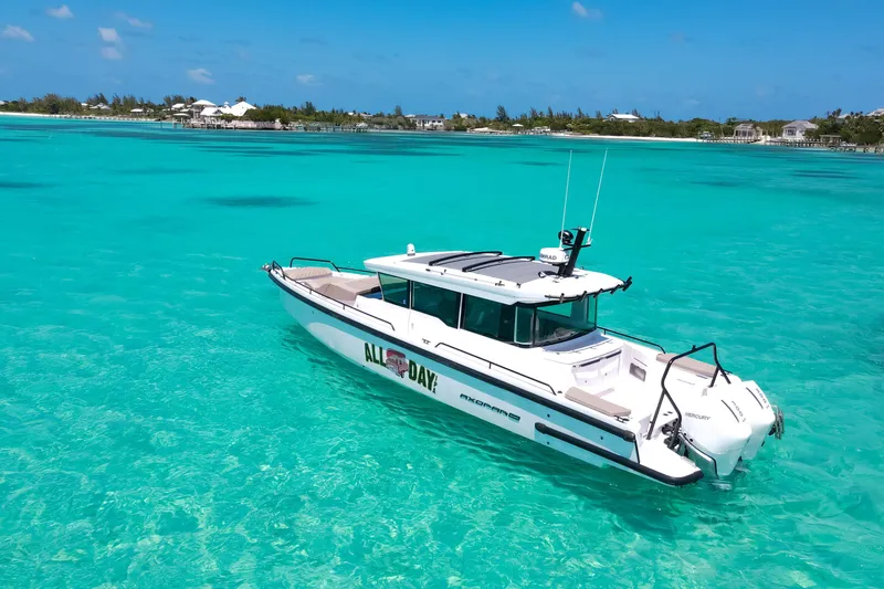 Slide: The Image of 2025 Axopar 37 XC Cross Cabin boat on clear turquoise water, near a tropical shoreline. - 2