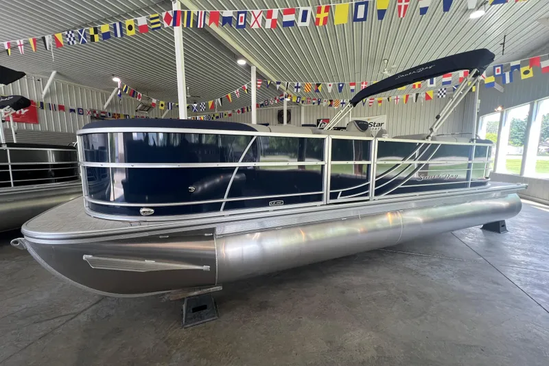 Slide: The Image of 2023 South Bay 224 RS pontoon boat displayed indoors with nautical flags above. - 20