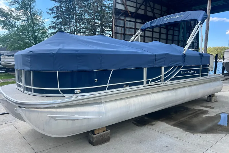 Slide: The Image of 2023 South Bay 224 RS pontoon boat with blue cover, docked in a marina. - 5