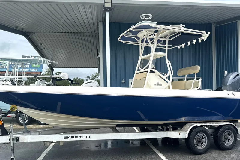 The Image of 2014 Skeeter SX2250 boat on trailer under shelter, featuring blue hull and T-top. - 1