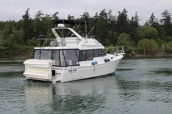 Slide: The Image of 1992 Bayliner 3288 Motoryacht cruising on a serene lake with forested shoreline. - 6