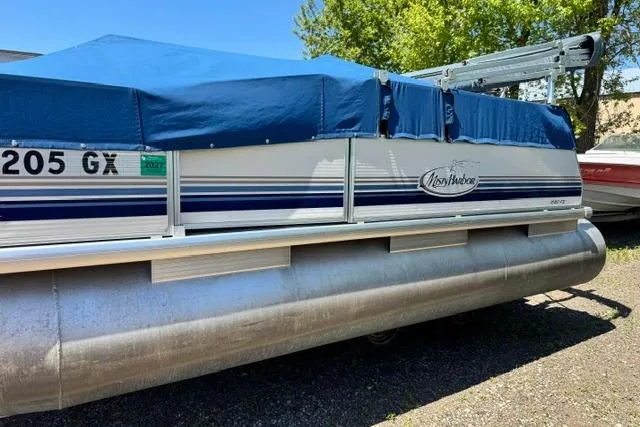 Slide: The Image of 2005 Misty Harbor 1680FS pontoon boat with blue cover, parked outdoors. - 2
