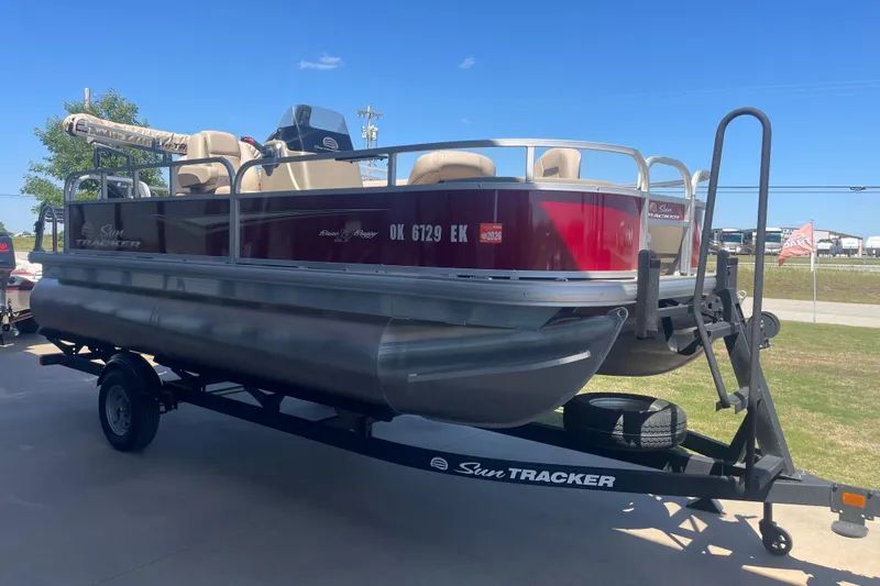 Slide: The Image of 2025 SUNTRACKER BASS BUGGY 18 pontoon boat on trailer, parked outdoors under clear blue sky. - 5