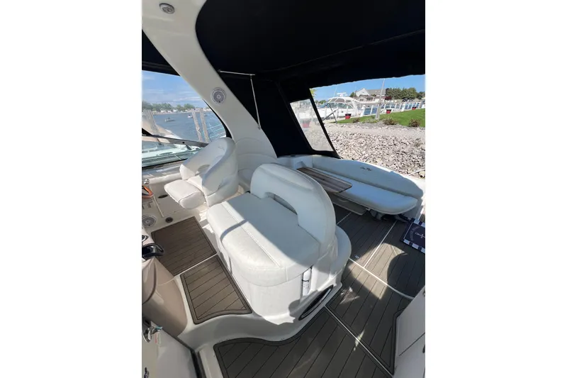 Slide: The Image of 2003 Sea Ray 360 Sundancer interior with white seating and wood accents, docked by the shore. - 12