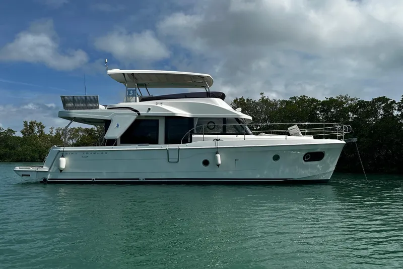 Slide: The Image of 2019 Beneteau Swift Trawler 47 on calm water, side view with lush greenery background. - 2