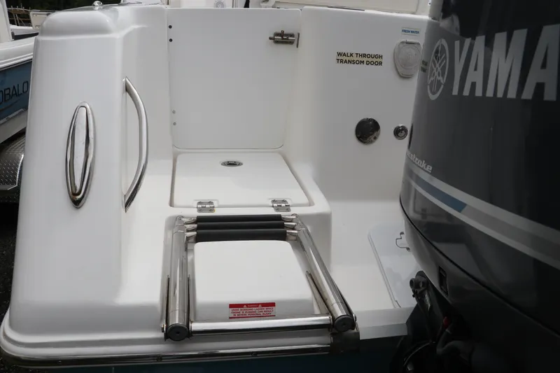 Slide: The Image of 2017 Tidewater 252 CC Adventure boat on trailer, parked near a wooded area. - 2