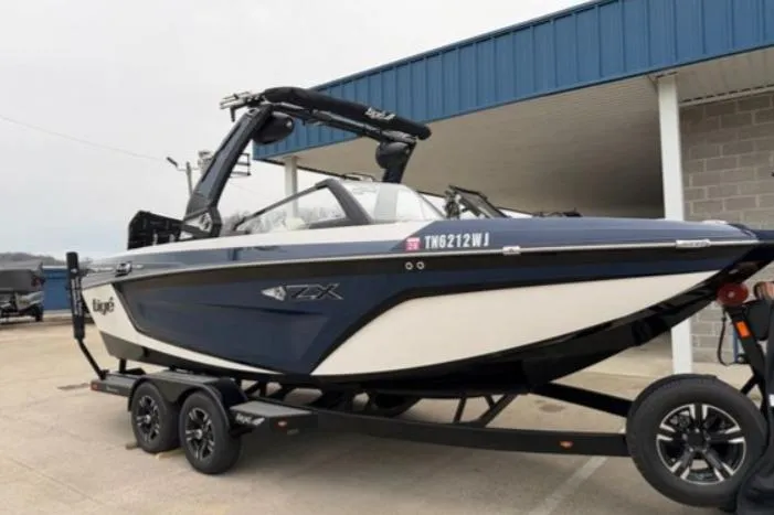 The Image of 2022 Tigé 21ZX boat on trailer, blue and white, parked outside a building. - 1