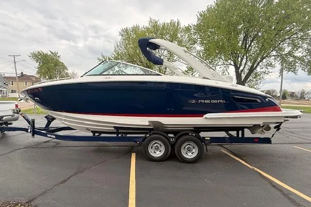 Slide: The Image of 2021 Regal 2800 Bowrider boat on trailer, parked in a lot with trees in the background. - 2