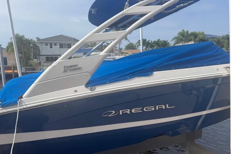Slide: The Image of 2024 Regal LX2 boat with blue cover and Power Tower, docked near waterfront homes. - 32