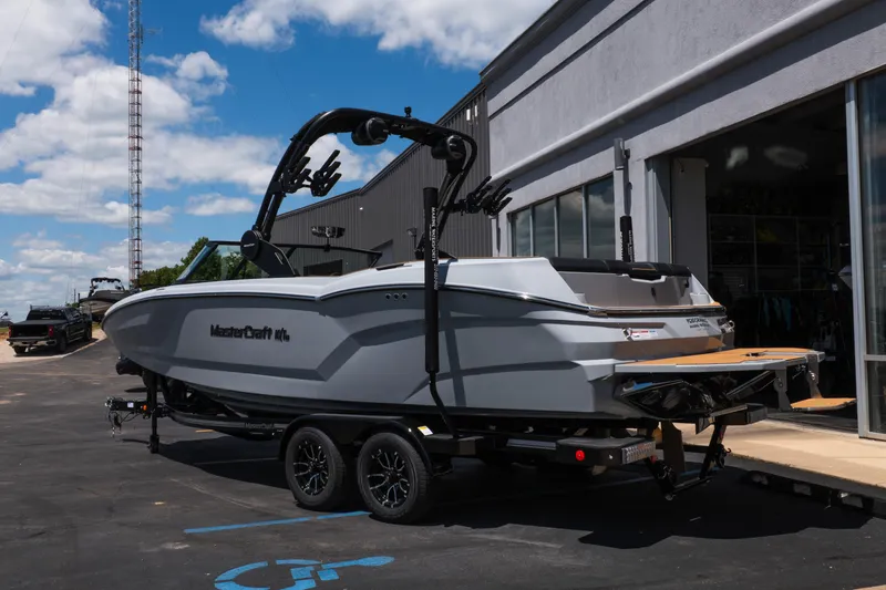 Slide: The Image of 2026 MasterCraft NXT24 boat on trailer outside a building under a blue sky. - 4