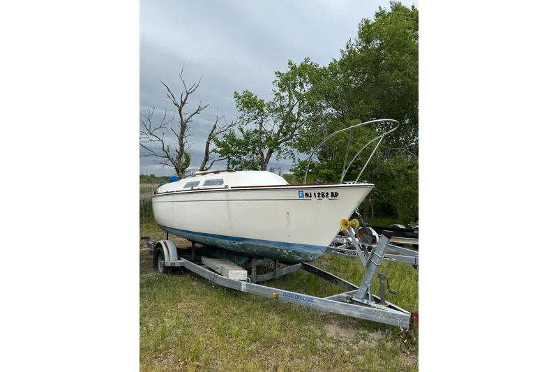 The Image of 1976 Paceship 23 sailboat on trailer, parked on grassy area with trees in background. - 0