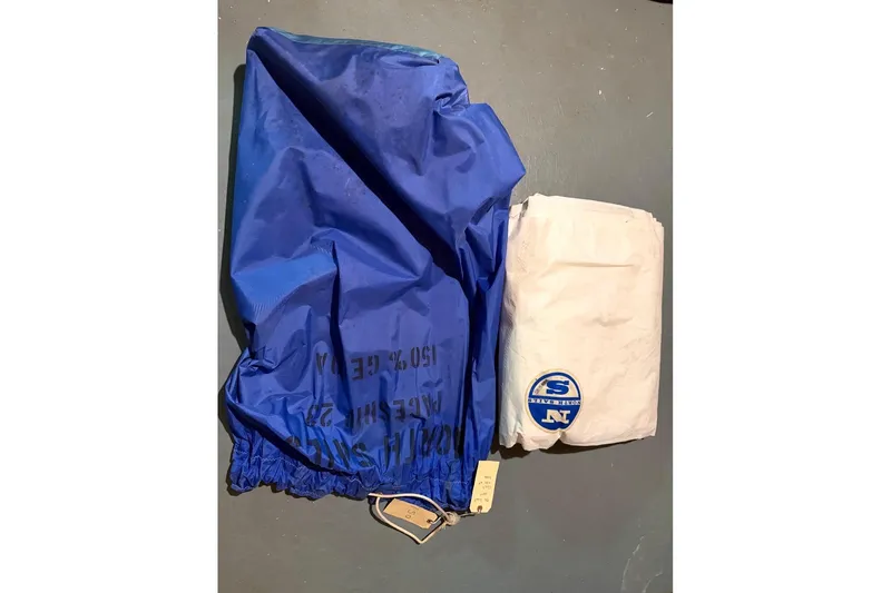Slide: The Image of Blue and white PAC 23 sailboat sails from 1976, neatly folded on a gray surface. - 12