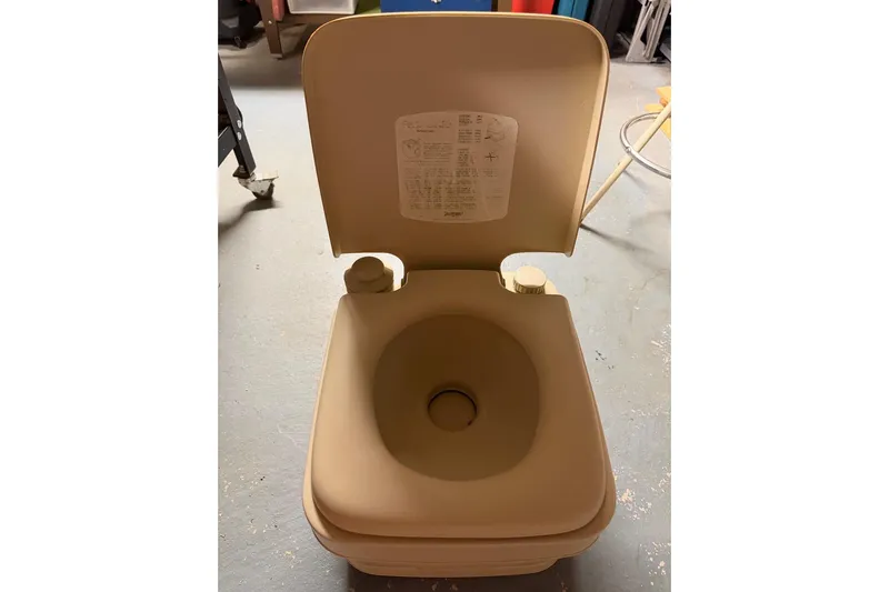 Slide: The Image of Vintage 1976 PAC 23 portable toilet with open lid, beige color, on a concrete floor. - 15