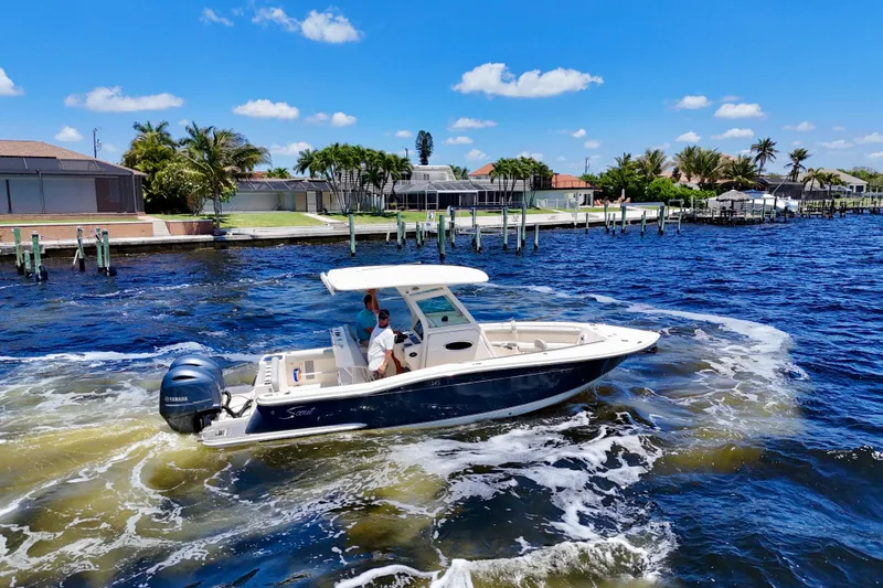Slide: The Image of 2023 Scout 255 LXF boat cruising on a sunny day near waterfront homes. - 7