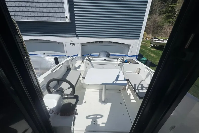 Slide: The Image of 2023 Jeanneau NC Sport 695 Series 2 boat interior with seating and table, parked near a house. - 23