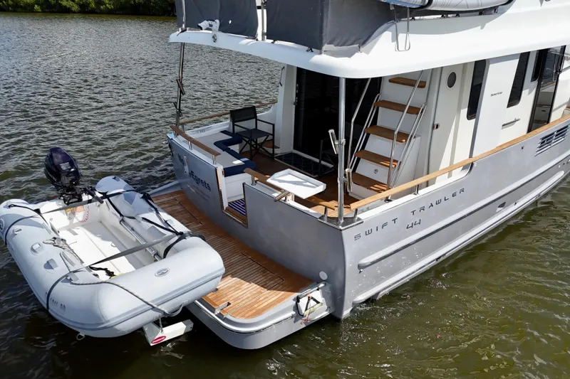 Slide: The Image of 2020 Beneteau Swift Trawler 44 with dinghy, docked on calm water. - 21