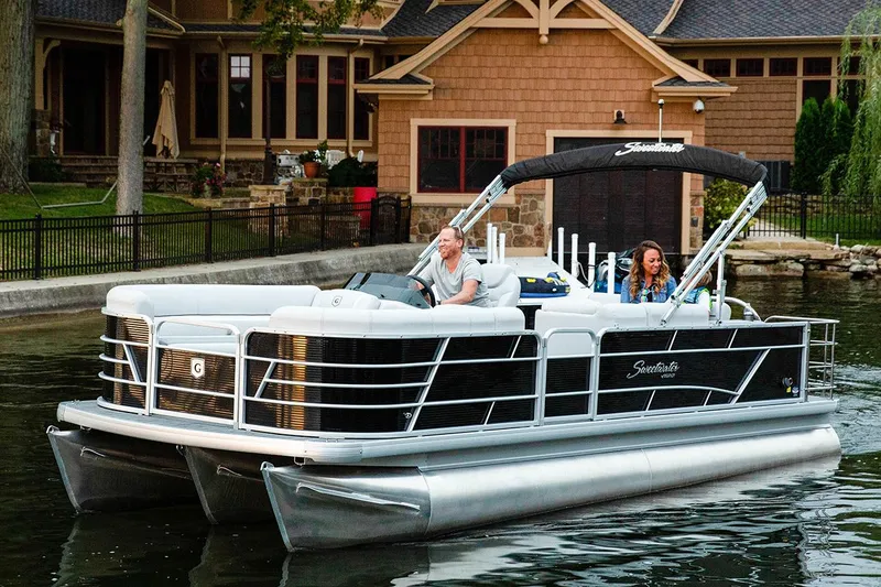 Slide: The Image of Manufacturer Provided Image: 2023 Godfrey SWEETWATER 2486 SFL pontoon boat cruising on a lake near a house. - 7