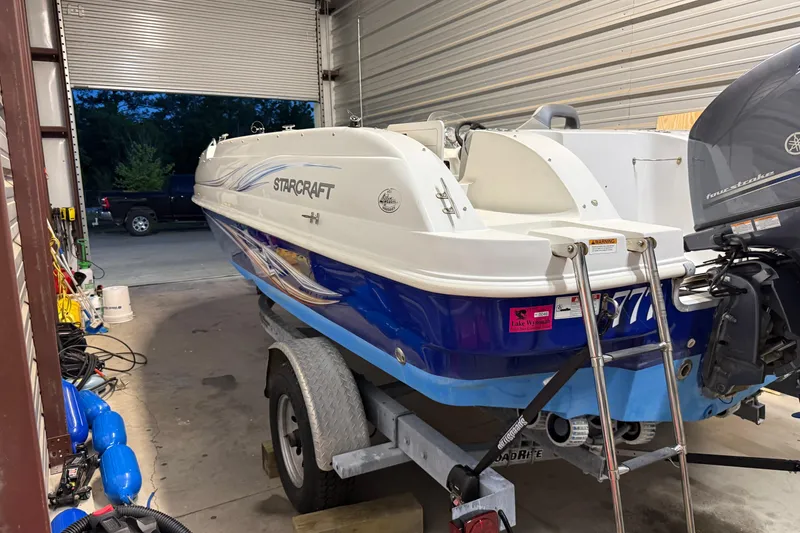 Slide: The Image of 2014 Starcraft 1915 OB Limited boat on trailer in garage, featuring blue and white design. - 7