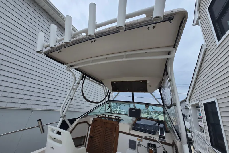 Slide: The Image of 1989 Sea Ox 250C boat cockpit with rod holders and steering wheel, docked between buildings. - 7