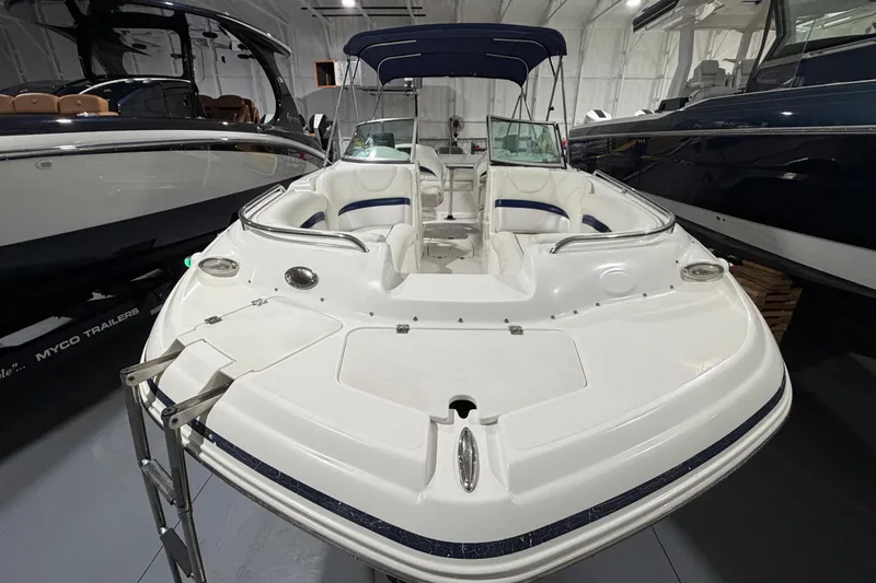 Slide: The Image of 2013 Hurricane SunDeck 2400 OB boat with white seating and blue accents in a showroom. - 9
