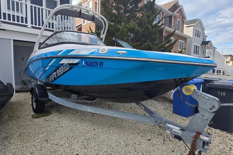 The Image of 2021 Yamaha Boats AR195 in blue, parked on a trailer near residential buildings. - 0