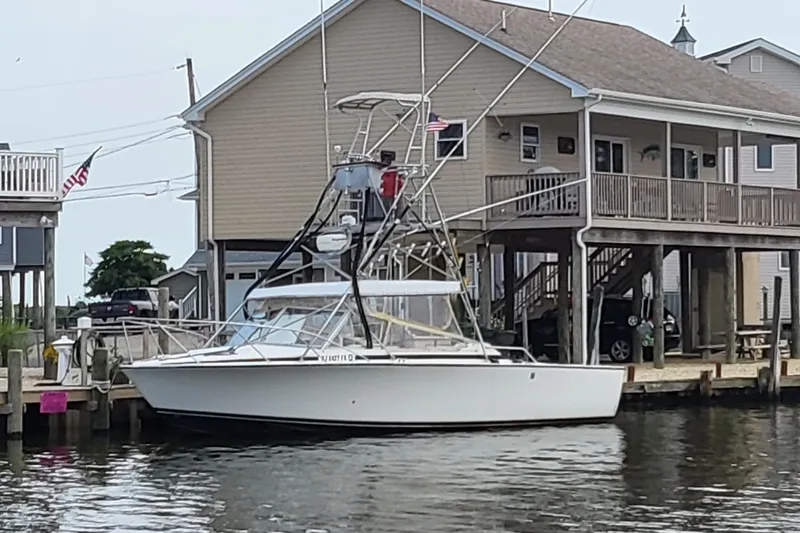 Slide: The Image of 1977 Bertram 28 Moppie boat docked near waterfront house, American flag visible. - 3