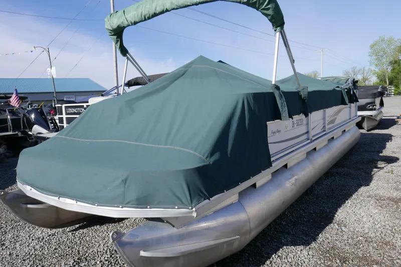 Slide: The Image of 2004 Sun Tracker Party Barge 240 pontoon boat with green cover, parked on gravel. - 2