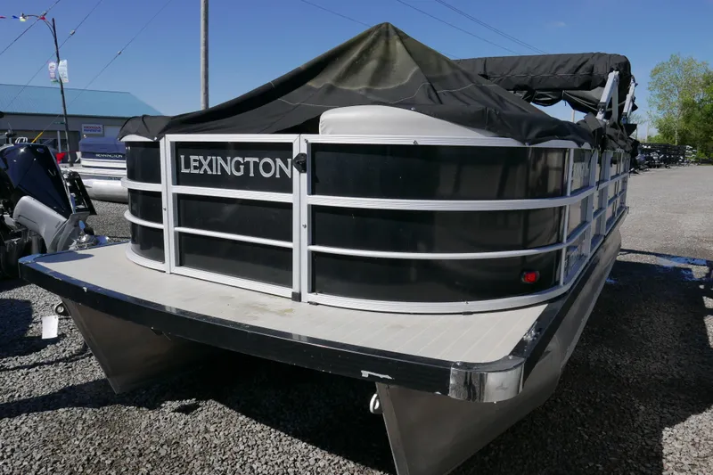 Slide: The Image of 2022 Lexington 320HPT pontoon boat with black cover, parked on gravel. - 2