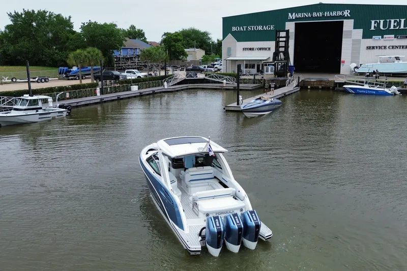 Slide: The Image of 2026 Formula 360 Crossover Bowrider OB navigating marina near boat storage facility. - 16