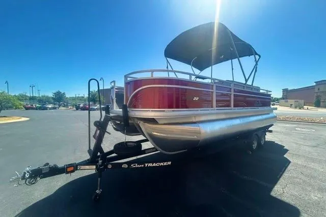 Slide: The Image of 2026 Sun Tracker Fishin' Barge 22 XP3 pontoon boat on trailer, parked outdoors. - 2