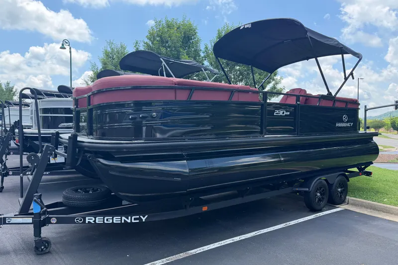 The Image of 2026 Regency 230 DL pontoon boat with red seating on a trailer, parked outdoors. - 0