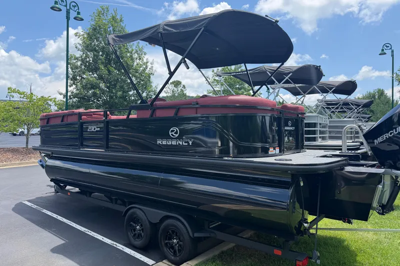 Slide: The Image of 2026 Regency 230 DL pontoon boat with canopy, parked on a trailer in a sunny outdoor setting. - 2