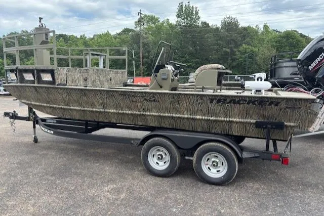 Slide: The Image of 2026 Tracker Grizzly 2072 CC Sportsman Kicker boat on trailer, camo design, parked outdoors. - 2