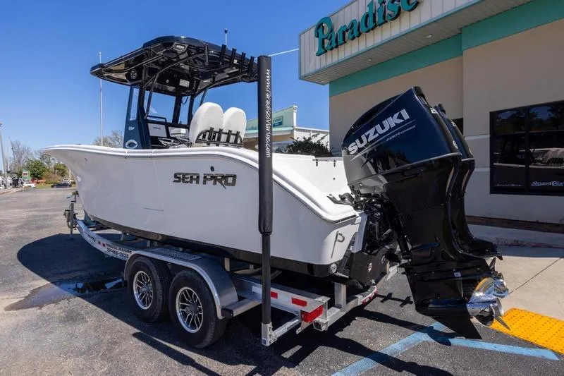 Slide: The Image of 2025 Sea Pro 262 Offshore boat on trailer with Suzuki outboard motor, parked outside a building. - 4