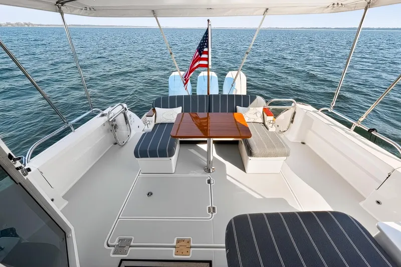 Slide: The Image of 2024 Back Cove 39O boat deck with seating, table, and American flag on open water. - 8