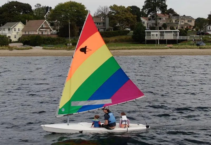 Slide: The Image of 2023 Dinghy Rocket Board Boat with colorful sail on the water near a residential shoreline. - 3