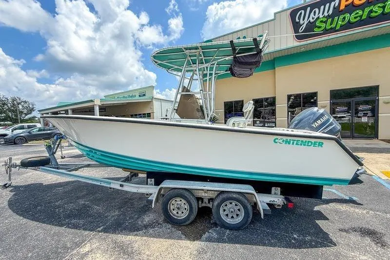 Slide: The Image of 1997 Contender 21 Open boat on trailer, parked outside a store under a blue sky. - 1