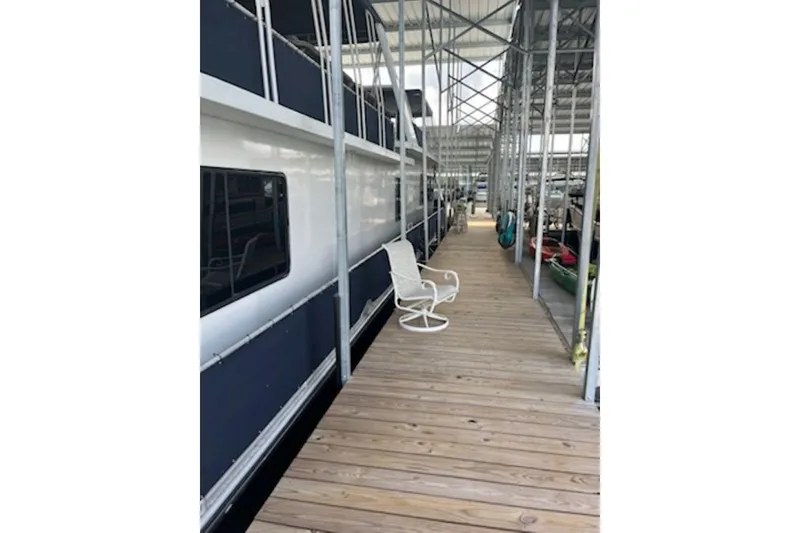 Slide: The Image of Docked 1985 Sumerset 18x81 houseboat with wooden walkway and white chair. - 30