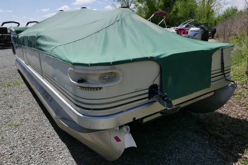 Slide: The Image of 2005 Bennington 257FS pontoon boat with green cover, parked on gravel. - 11
