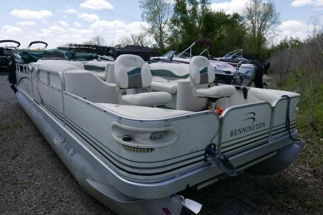 Slide: The Image of 2005 Bennington 257FS pontoon boat parked on gravel, surrounded by trees and other boats. - 2