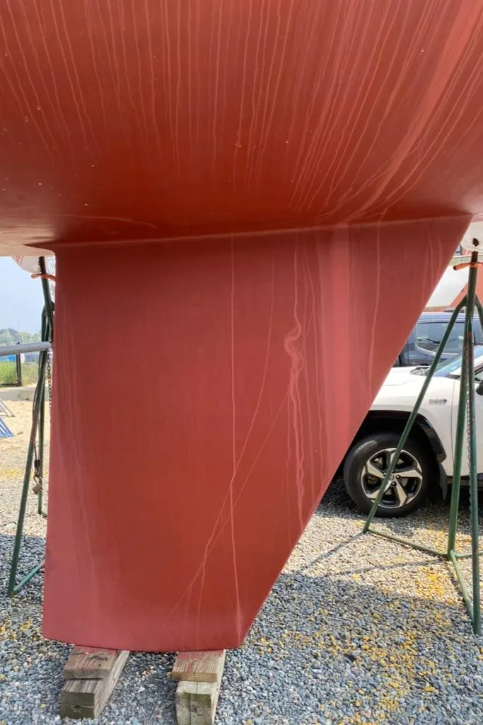 Slide: The Image of Red hull of 1986 Express 37 sailboat on stands, gravel ground. - 7