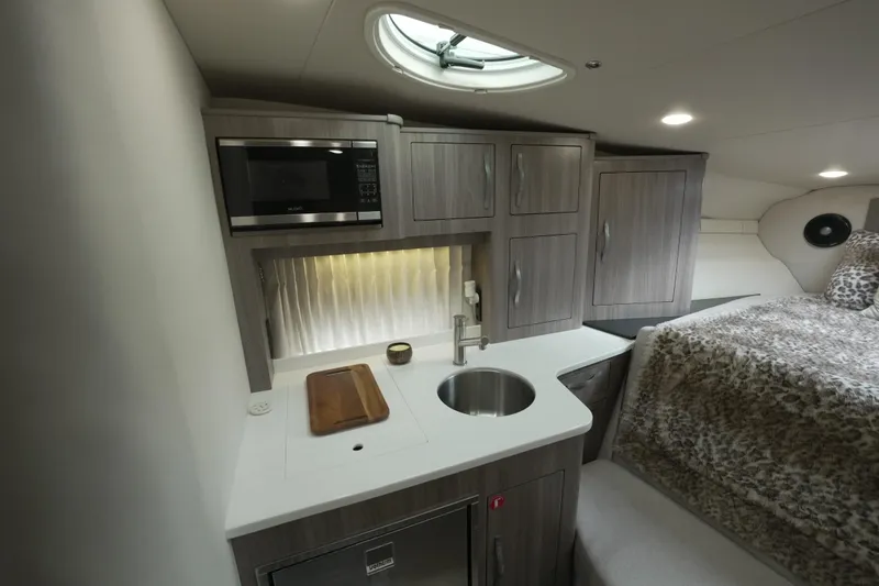 Slide: The Image of 2021 Regal 33 XO yacht interior with kitchenette, microwave, sink, and cozy sleeping area. - 16