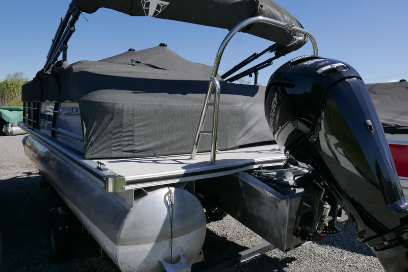 Slide: The Image of 2023 Trifecta C Series pontoon boat with Mercury outboard motor, covered and parked on gravel. - 17