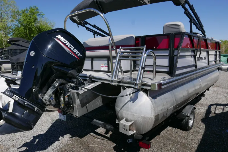 Slide: The Image of 2023 Trifecta C Series pontoon boat with Mercury outboard motor, parked on gravel. - 3