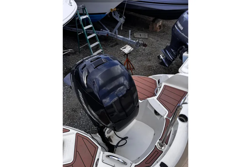 Slide: The Image of 2015 Stingray 234 LR boat with outboard motor, parked on gravel with ladder nearby. - 16