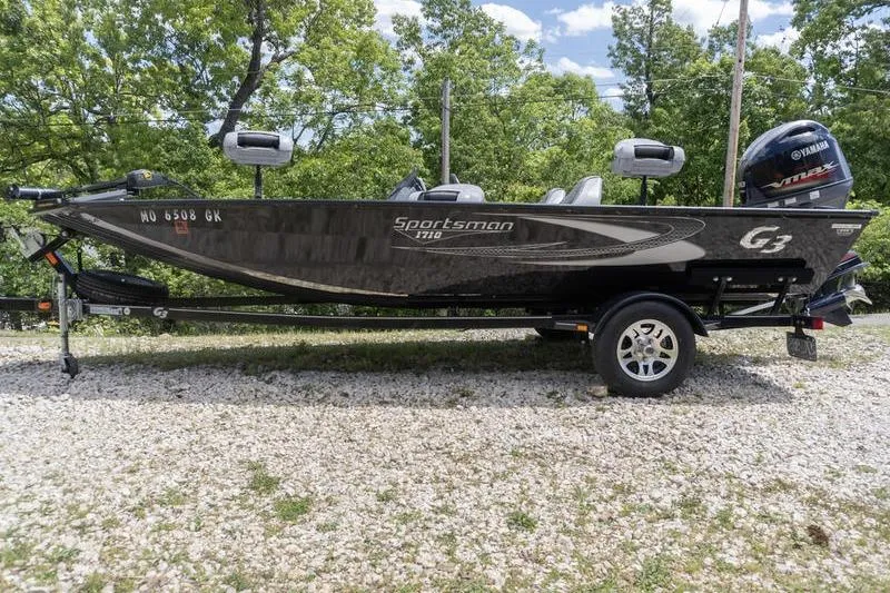 The Image of 2019 G3 Sportsman 1710 boat on trailer, surrounded by trees and gravel. - 1