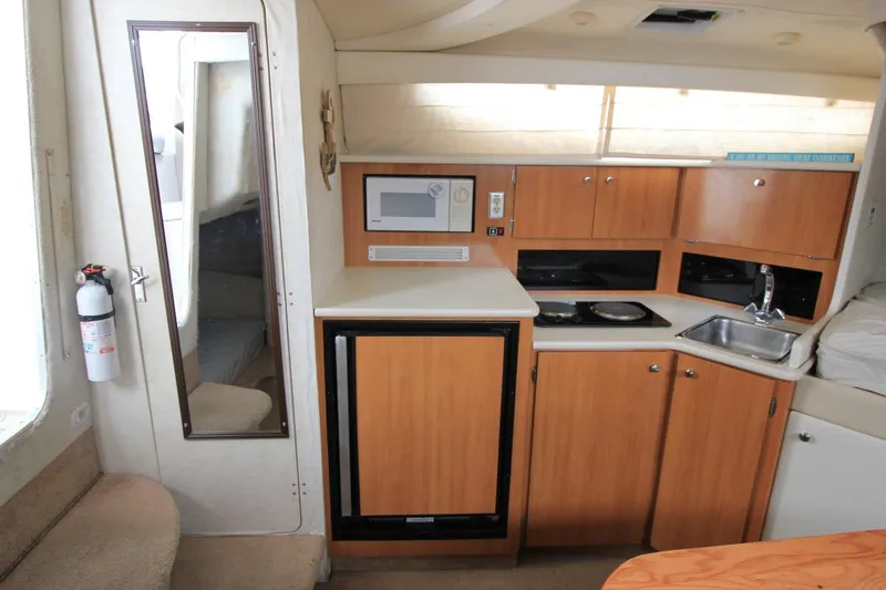 Slide: The Image of 2001 Bayliner 3055 Ciera interior with kitchenette, featuring microwave, sink, and wooden cabinets. - 19