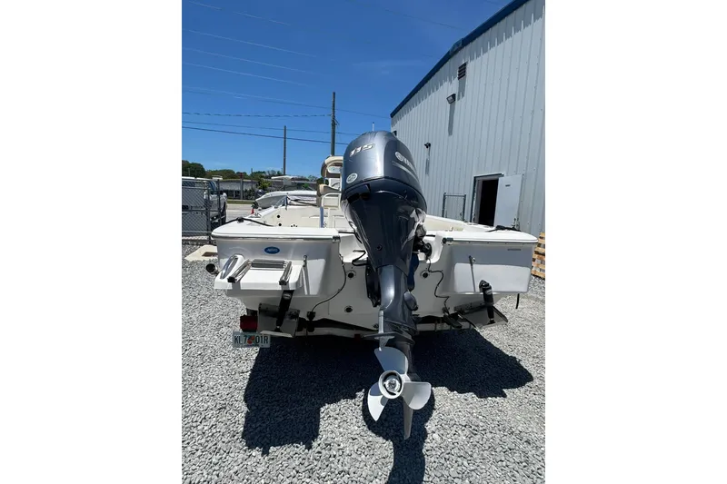 Slide: The Image of 2018 Tidewater 1910 Bay Max boat with outboard motor, parked on gravel near a building. - 12